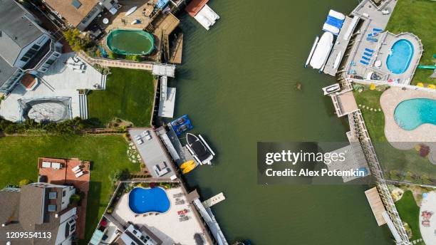 top view, directly above drone photos of a channel in oceanside, new york city, with houses with pools on backyards and piers with boats along the shore. - oceanside pier stock pictures, royalty-free photos & images
