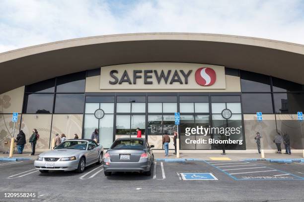 Customers, some wearing protective masks and gloves, wait in a line outside a a Safeway Inc. Store, operated by Albertsons Cos. Inc., in San...