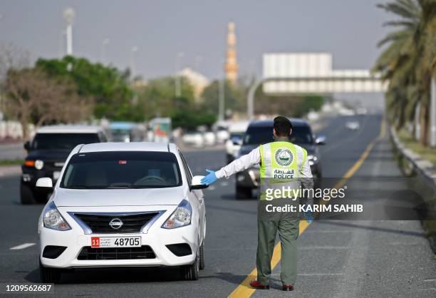 Policeman stops vehicles at a security checkpoint to examine passengers for exit permits, as people are only allowed essential travel due to a...