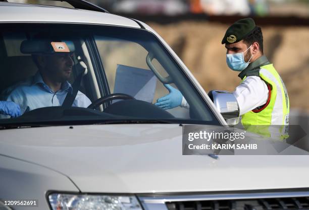 Policeman stops vehicles at a security checkpoint to examine passengers for exit permits, as people are only allowed essential travel due to a...