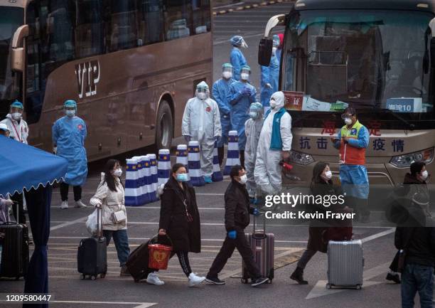 Chinese workers and health officials wear protective suits as they watch travellers from Hubei province, including Wuhan, as they gather to take...