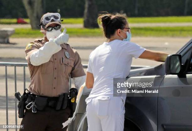 Un trabajador de la salud, junto a un policía de Miami-Dade, revisa los datos personales de un conductor en la fila de vehículos, mientras este...