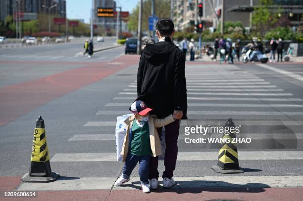 Man leading a face mask-clad child waits to cross a street in Beijing on April 11 amid the COVID-19 coronavirus pandemic.