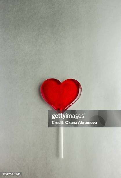 red heart-shaped lollipop on a colored plain background - lollipop fotografías e imágenes de stock