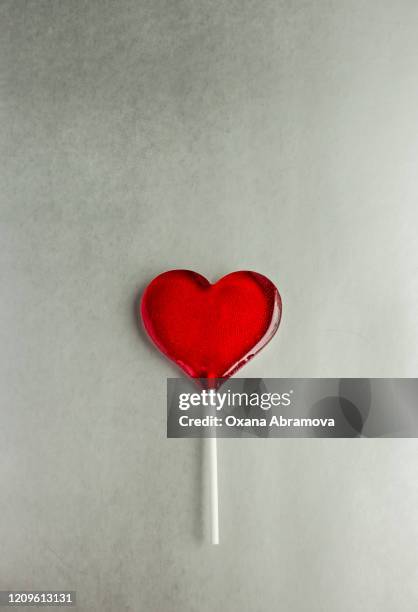 red heart-shaped lollipop on a colored plain background - lolly stockfoto's en -beelden