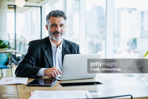 homme d’affaires barbu de sourire travaillant sur l’ordinateur portatif dans le bureau - homme d'affaires photos et images de collection
