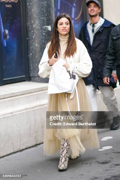 Guest wears a beige turtleneck, a white leather jacket, a beige flowing asymmetric tutu skirt, a white bag, beige and black python patterned pointy...