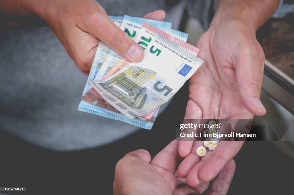 Close up of hand with money buying party pills with smily face from dealer
