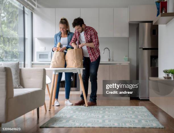 couple unpacking groceries at home - young man groceries kitchen stock pictures, royalty-free photos & images