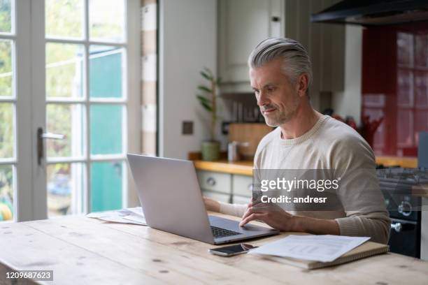 man working at home on his laptop computer - study older man imagens e fotografias de stock