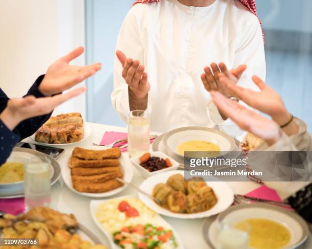 muslim family praying during having iftar in ramadan together - arab family in hotel stock-fotos und bilder