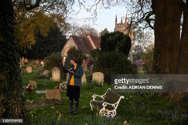 Priest-in-Charge Angie Smith, uses her smartphone to live-broadcast an Easter Sunday service to her congregation at dawn, from the churchyard of Old...