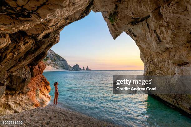 young woman enjoying the sunrise from a cave at two sisters beach (le due sorelle). conero, italy - natural arch stock pictures, royalty-free photos & images