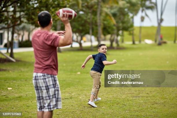 hispanic father throwing football to young son in miami - boy looking over shoulder stock pictures, royalty-free photos & images