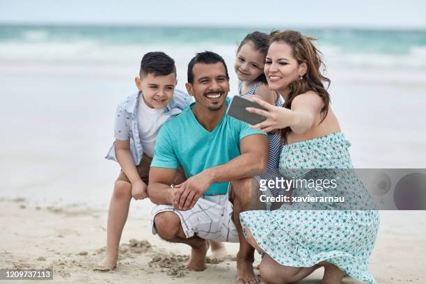 sorglose hispanische familie macht selfie des tages am strand - hispanic man on beach stock-fotos und bilder