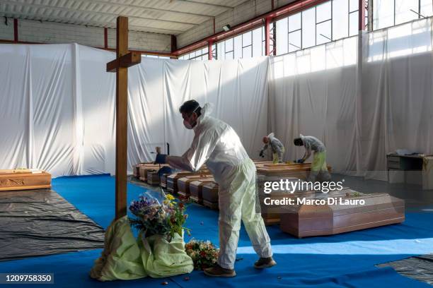 Member of the Civil Protection service collects a flower to rest on the coffin of a victim of COVID-19 in the hangar where 18 coffins wait to be...