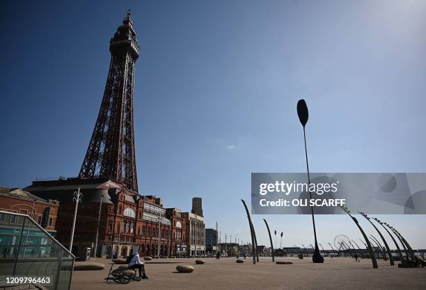 People walk along the promenade near the Blackpool Tower in the spring sunshine on the coast in Blackpool, north-west England on April 13 during the...