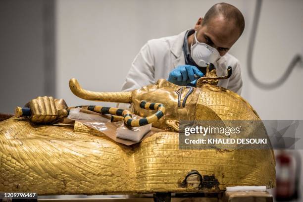 An Egyptian archeologist, wearing personal protective equipment, performs restorations on the golden sarcophagus of the ancient Egyptian Pharaoh...