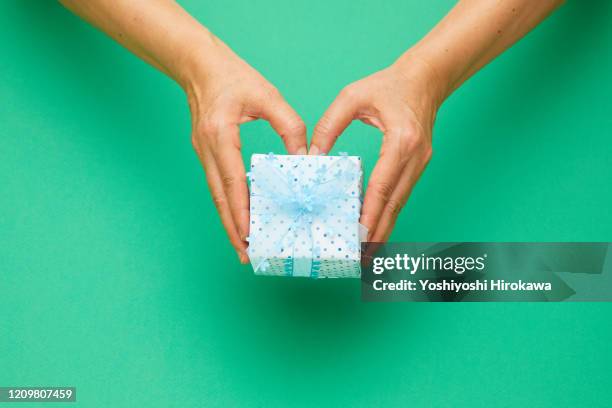 holding blue wrapped craft paper gift on green.heart shaped hands. - お中元 ストックフォトと画像