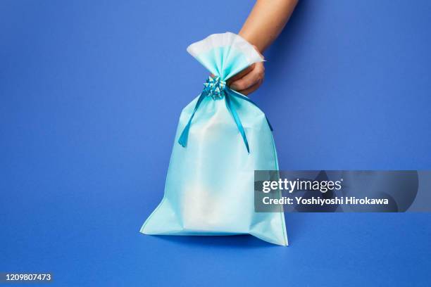 hands holding blue wrapped craft paper gift on blue - hohlkehle stock-fotos und bilder