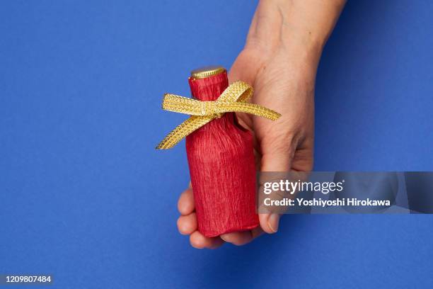 holding wrapped whiskey bottle gift on blue. - hohlkehle stock-fotos und bilder