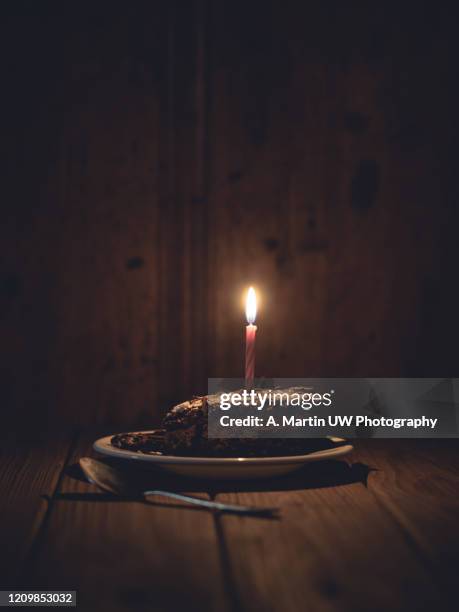 slice of chocolate cake with one birthday candle on an old wood table - candle white background stock-fotos und bilder