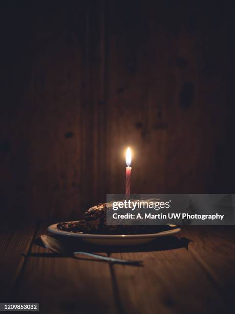 slice of chocolate cake with one birthday candle on an old wood table - pastel intensidad del color fotografías e imágenes de stock