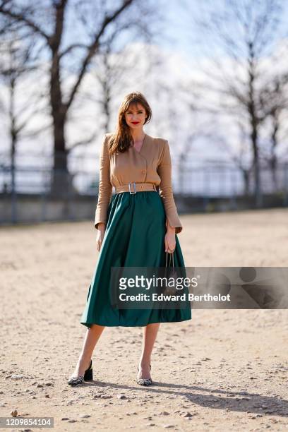 Julie Ianc wears a green skirt, a bag, a brown double breasted top with buttons and shoulder pads, a belt, black and white zebra print pattern shoes,...