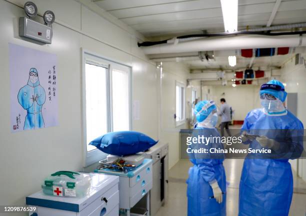 Medical workers talk with each other next to a caricature painting at the Huoshenshan makeshift hospital on March 2, 2020 in Wuhan, Hubei Province of...