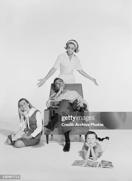 Woman standing behind man sitting on chair, children playing around