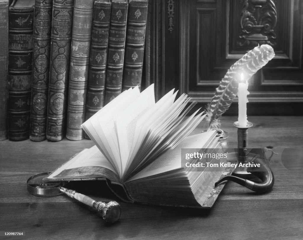 Open book with feather pen, inkpot, magnifying glass and candle