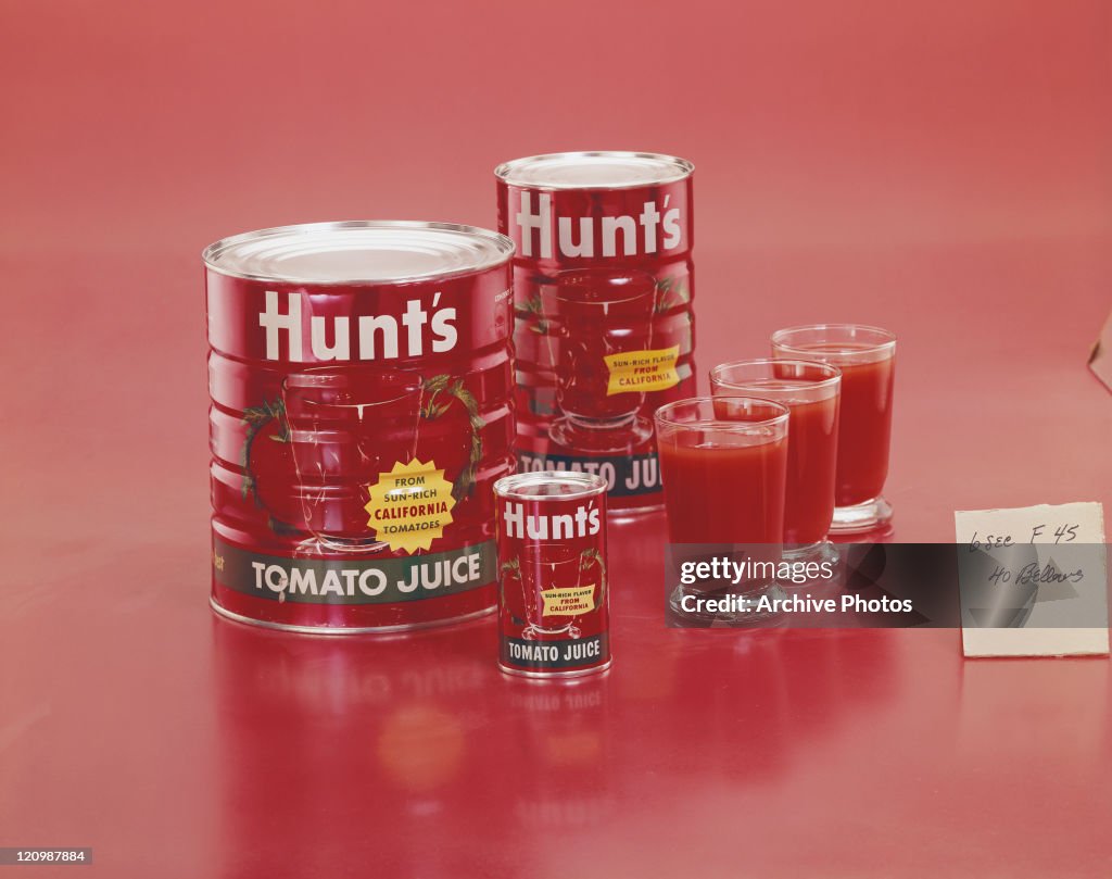 Tin cans of tomato sauce with glasses on red background