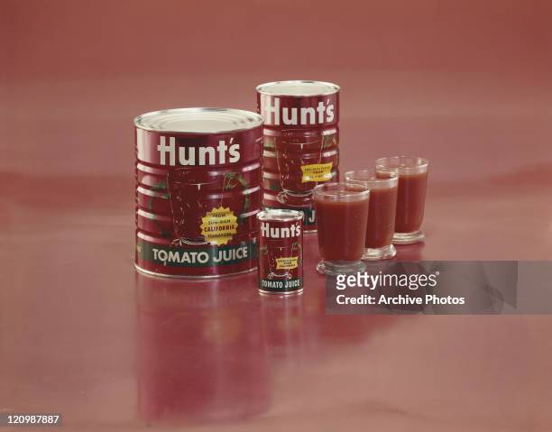 Tin cans of tomato sauce with glasses on red background
