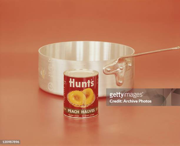 Tin of peach halves with pan on orange background, close-up