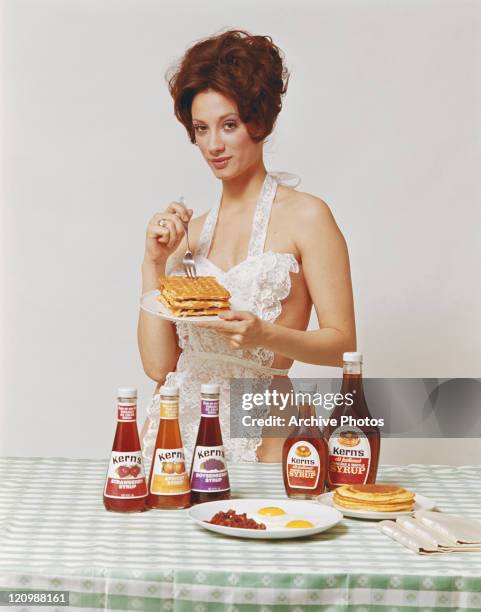Young woman in apron holding waffles with fruit syrups in front, portrait