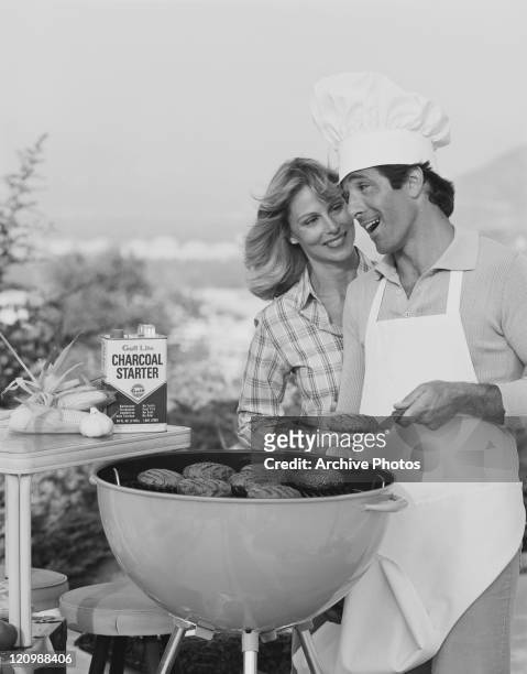 Couple standing beside barbecue grill, smiling