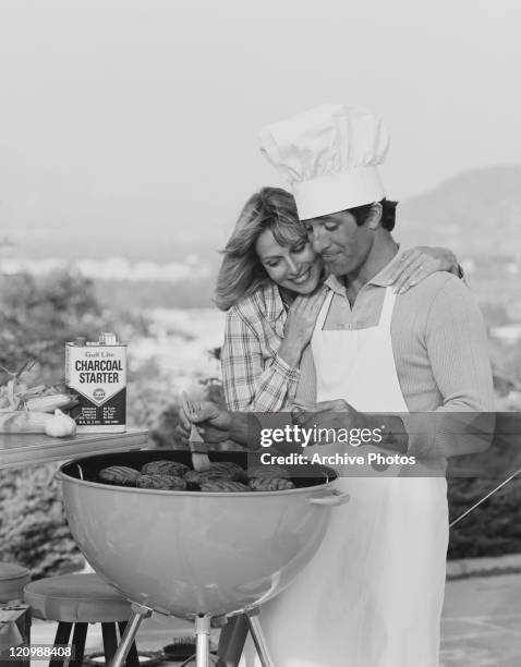 Man basting barbecue with brush and woman watching