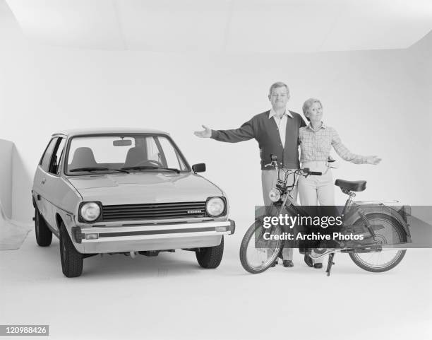 Mature couple standing beside Ford Fiesta and Puch moped, smiling, portrait