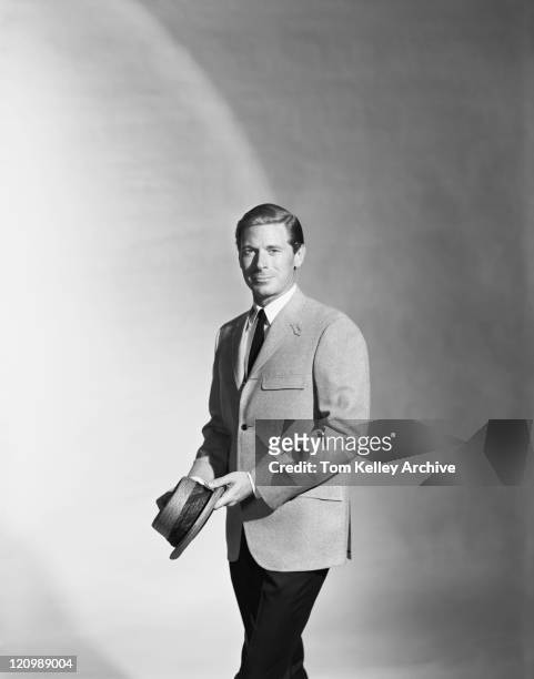 hombre que agarra sombrero de pie contra un fondo gris, vertical - años 60 fotografías e imágenes de stock
