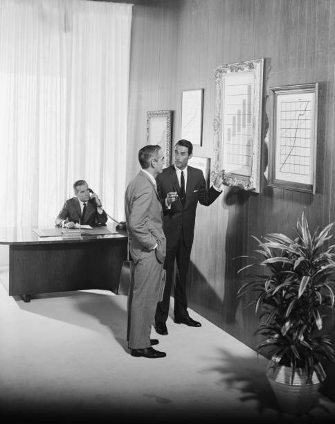 Two businessman discussing at bar chart while another man using telephone in background