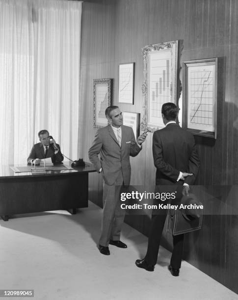 two businessman discussing at bar chart while another man using telephone in background - archive the office stockfoto's en -beelden