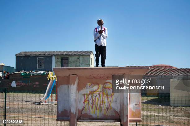 Man stands on a bus shelter and prays during clashes between the South African Police Service and residents of Tafelsig, an impoverished suburb in...
