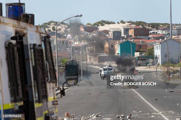 Armoured vehicles belonging to the South African Police Services and the Cape Town Metro Police drive past a burning barricade during clashes with...