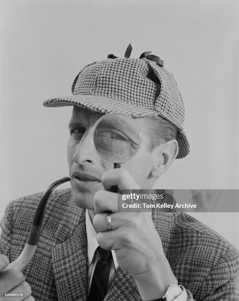 Man holding pipe and looking through magnifying glass