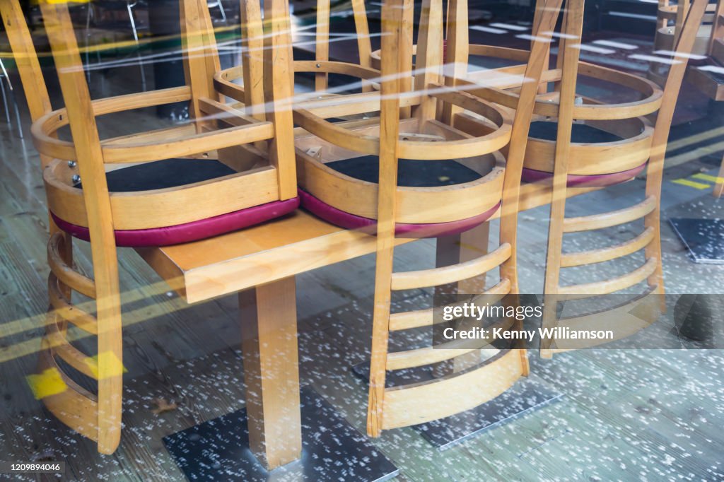 Looking through a closed bar window from the street to chairs upside down on a table