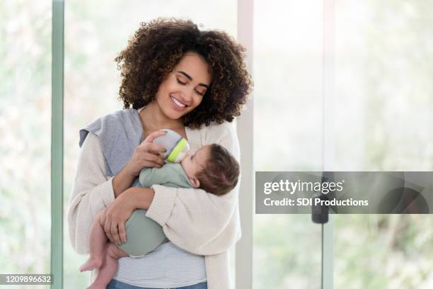lächelnde neue mutter füttert baby junge - milchpulver stock-fotos und bilder