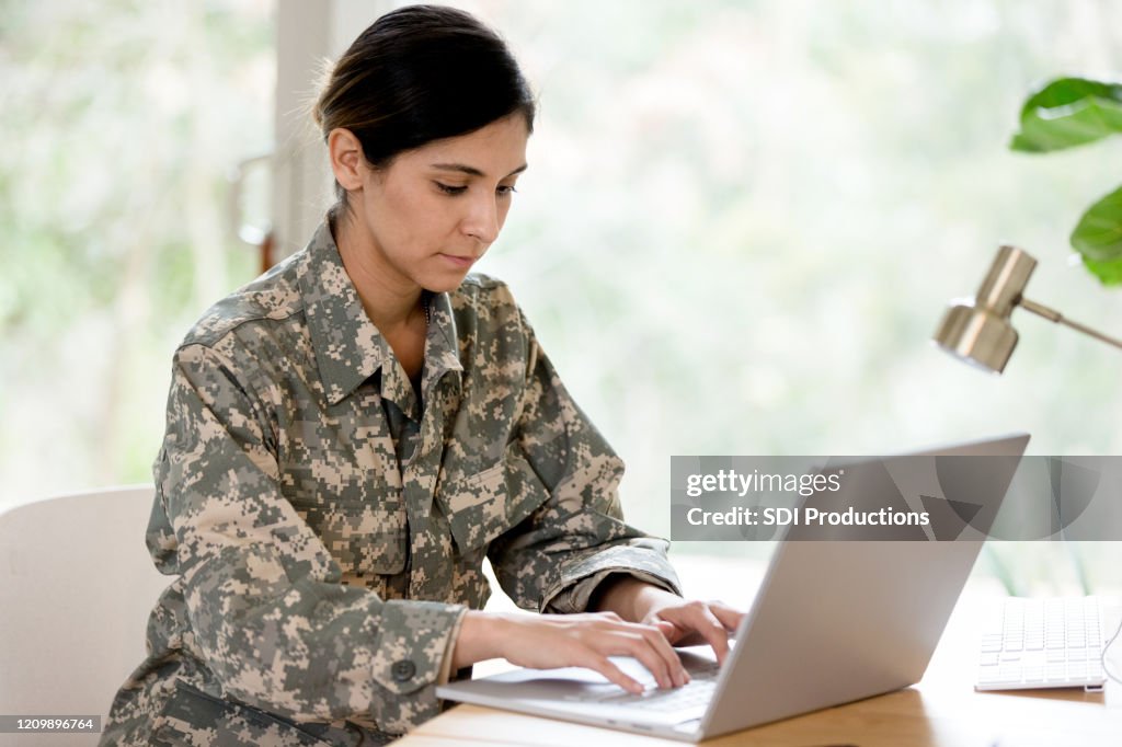 Soldado de mediana adulta trabaja en la computadora portátil en casa