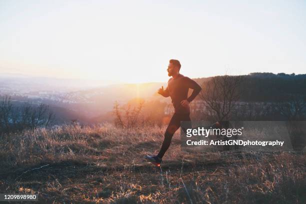 mann läuft bei sonnenuntergang über die stadt - winter sport stock-fotos und bilder
