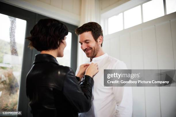 young woman helping her smiling husband button his shirt - buttoning stock pictures, royalty-free photos & images