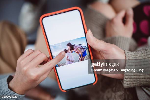 close-up of mom & daughter’s hands using smartphone together - album de photographies photos et images de collection